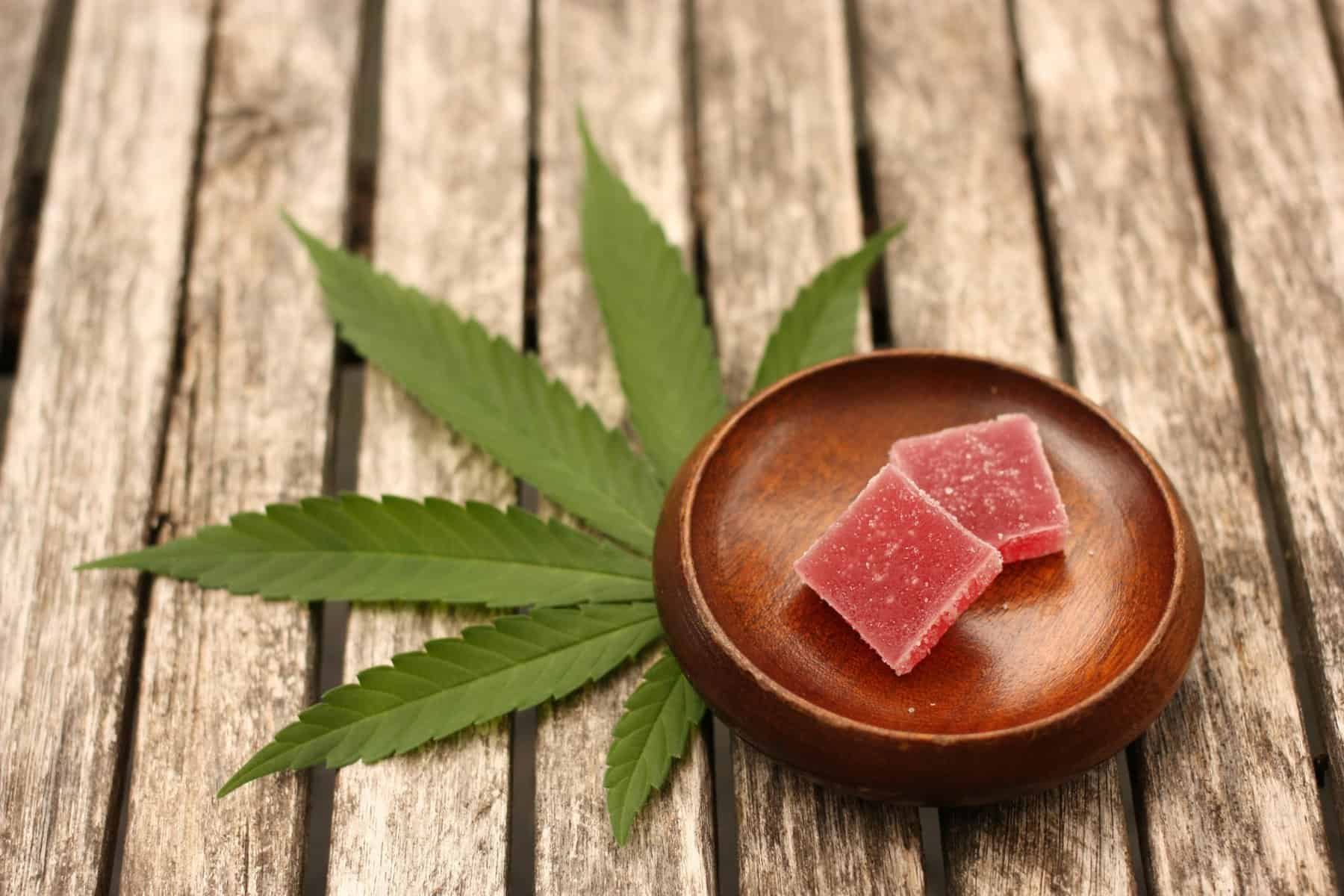 Cannabis leaf under wooden tray with thc gummy
